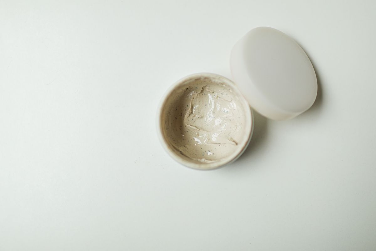 White cream texture swatch on a gray surface beside an unlabeled skincare tube