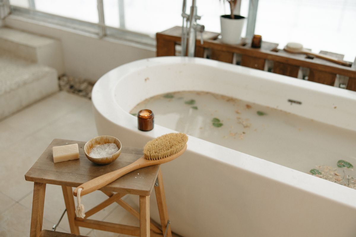 White bathtub filled with water beside a jar of bath salts and folded towels