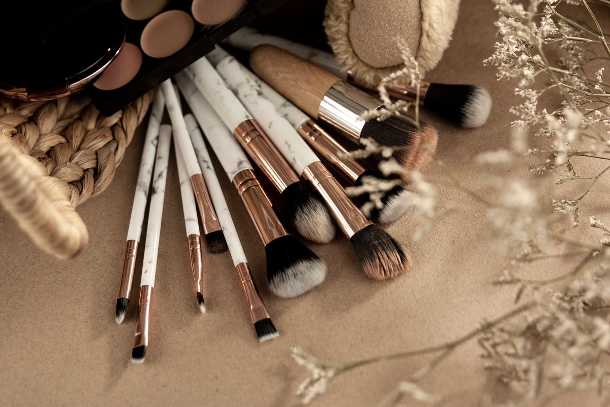 Makeup brushes resting beside an eyeshadow palette on a beige surface