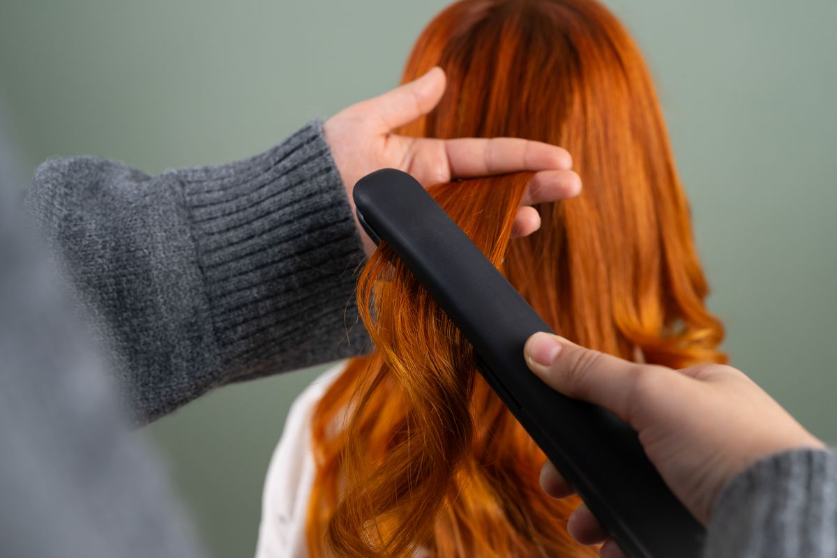 Flat iron styling long red hair with a heat-resistant glove