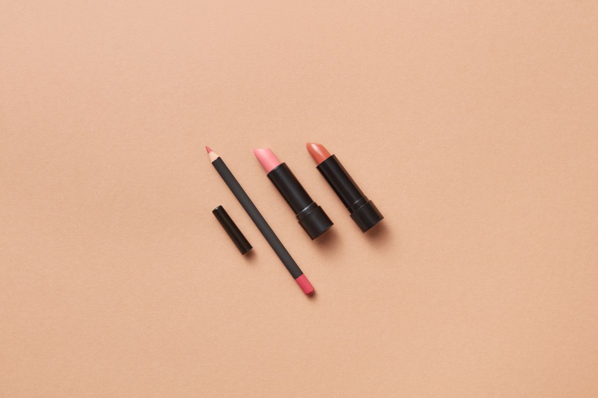 A pink lipstick beside an orange lip balm on a flat surface