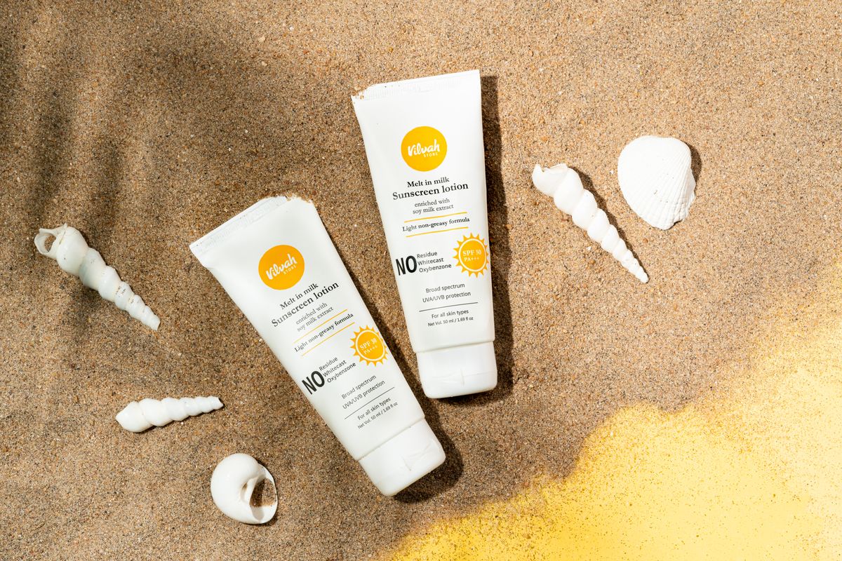Tubes of sunscreen lying on sand between seashells
